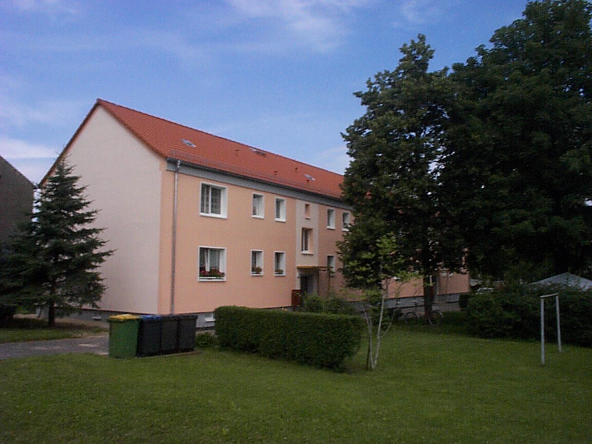 Ansicht eines zweistöckigen sanierten Mehrfamilienhauses im grünen Grundstück mit großen Bäumen