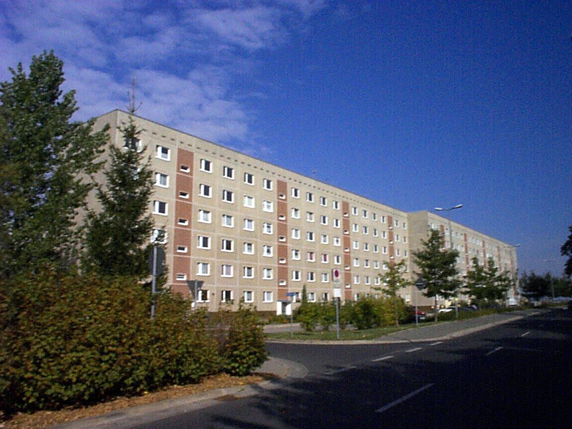 Straßenansicht eines sechsstöckigen unsanierten Mehrfamilienhauses im grünen Grundstück