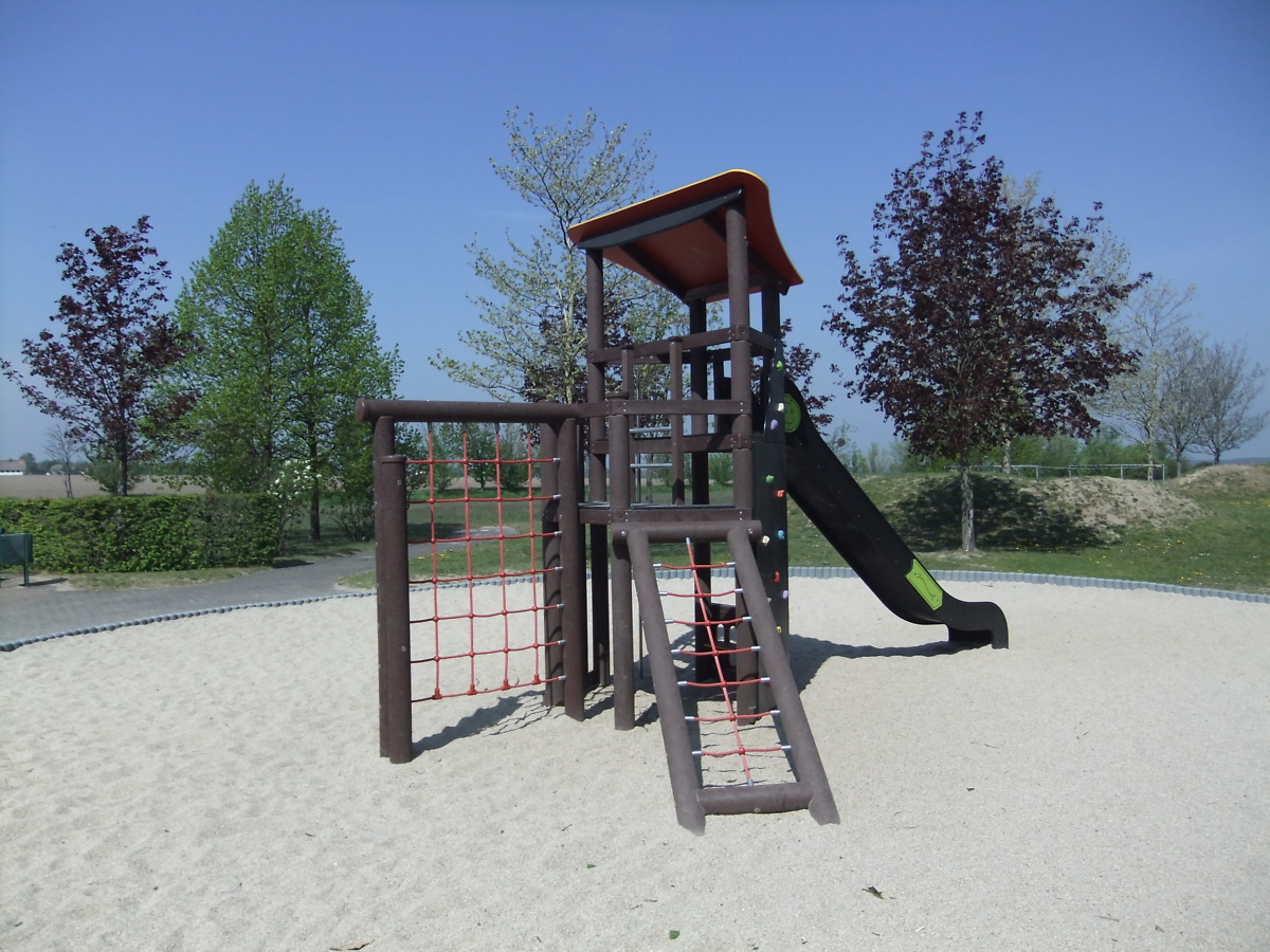 Blick auf einen Kletterturm mit Rutsche auf großer Sandfläche im grünen Grundstück