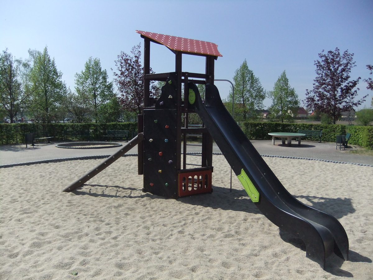 Blick auf einen Kletterturm mit Rutsche auf großer Sandfläche im grünen Grundstück