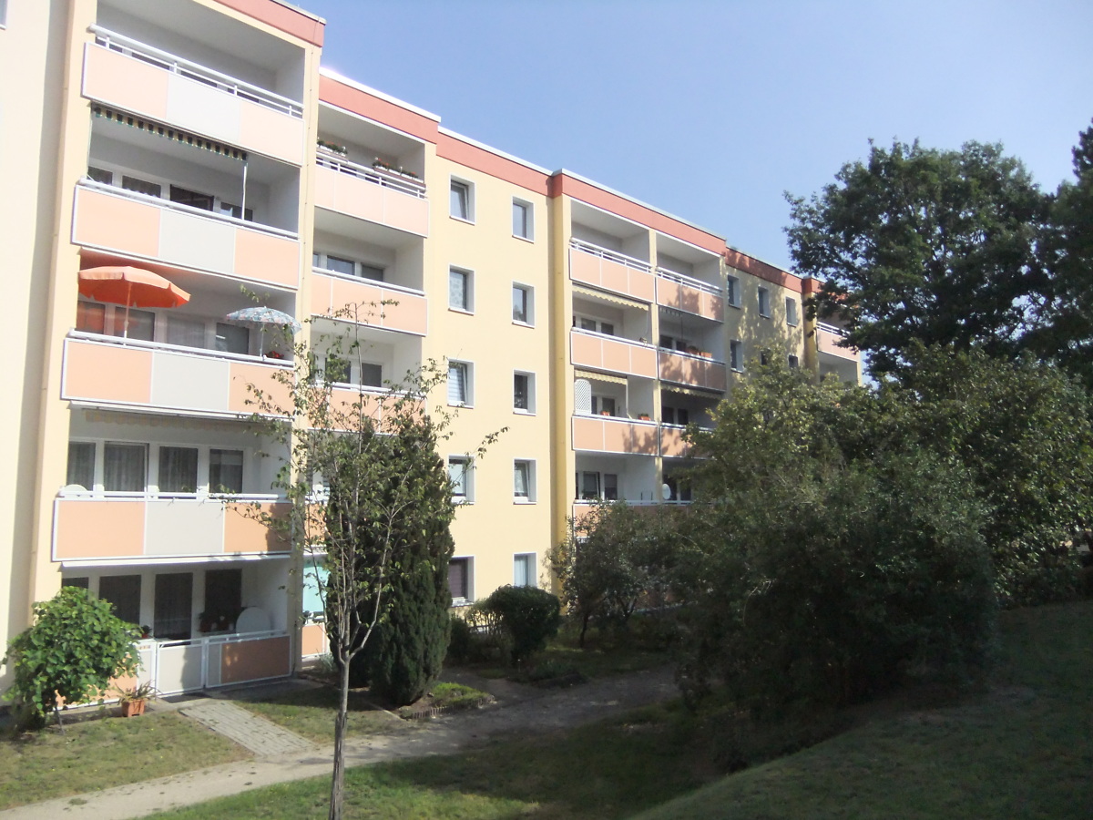 Ansicht eines fünfstöckigen sanierten Mehrfamilienhauses im grünen Grundstück mit Balkonen