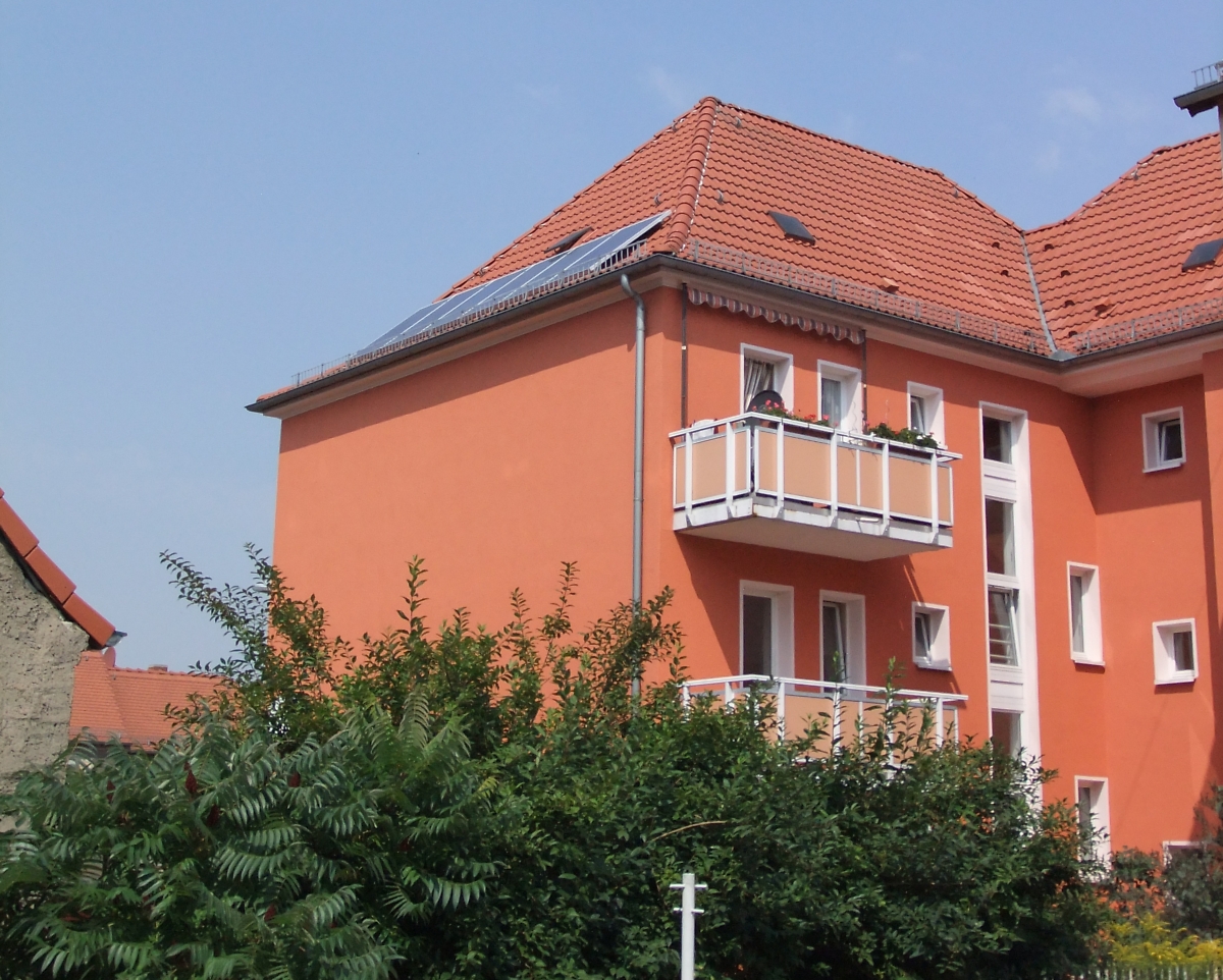 Ansicht eines dreistöckigen sanierten Mehrfamilienhauses im grünen Grundstück mit Balkonen